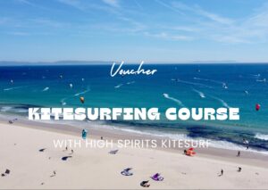 Osoba trzymająca voucher High Spirits Kite/Surf Kurse na plaży w Tarifie, z kitesurferami w tle.