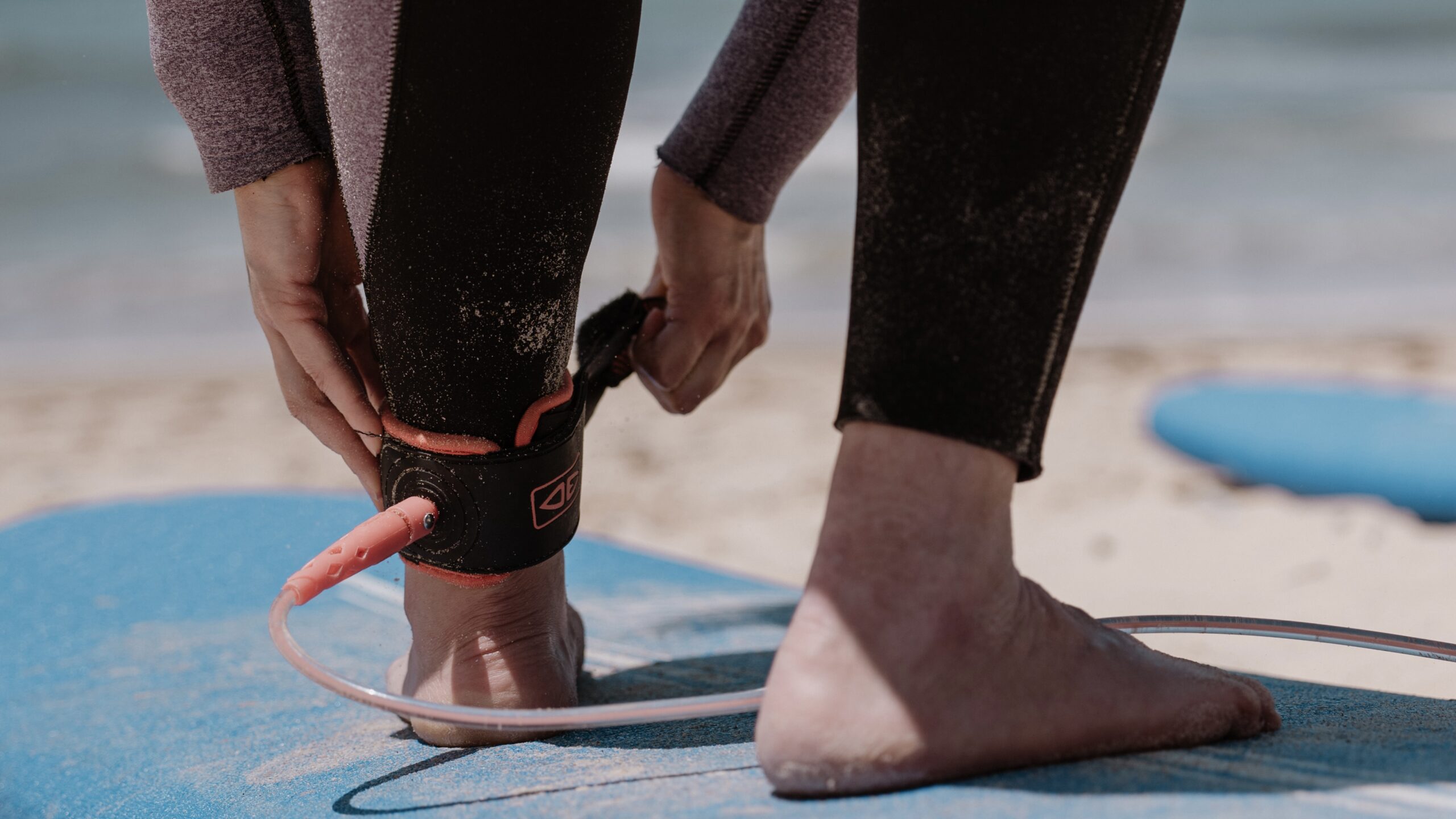 Kursantka zakładająca leash przed wejściem do wody podczas lekcji surfingu w Tarifie. 